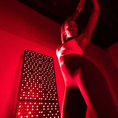 Woman stretching in a red-lit room with a red light therapy panel in the background.
