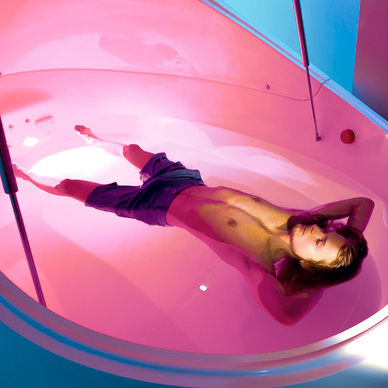 Man floating in float tank with pink light on